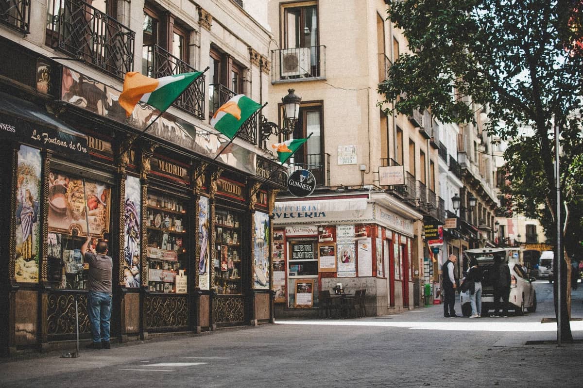 Charmante Straßenszene in Madrid mit alten Ladenfronten, Fahnen und Straßencafés unter Bäumen, perfekt für einen romantischen Spaziergang.
