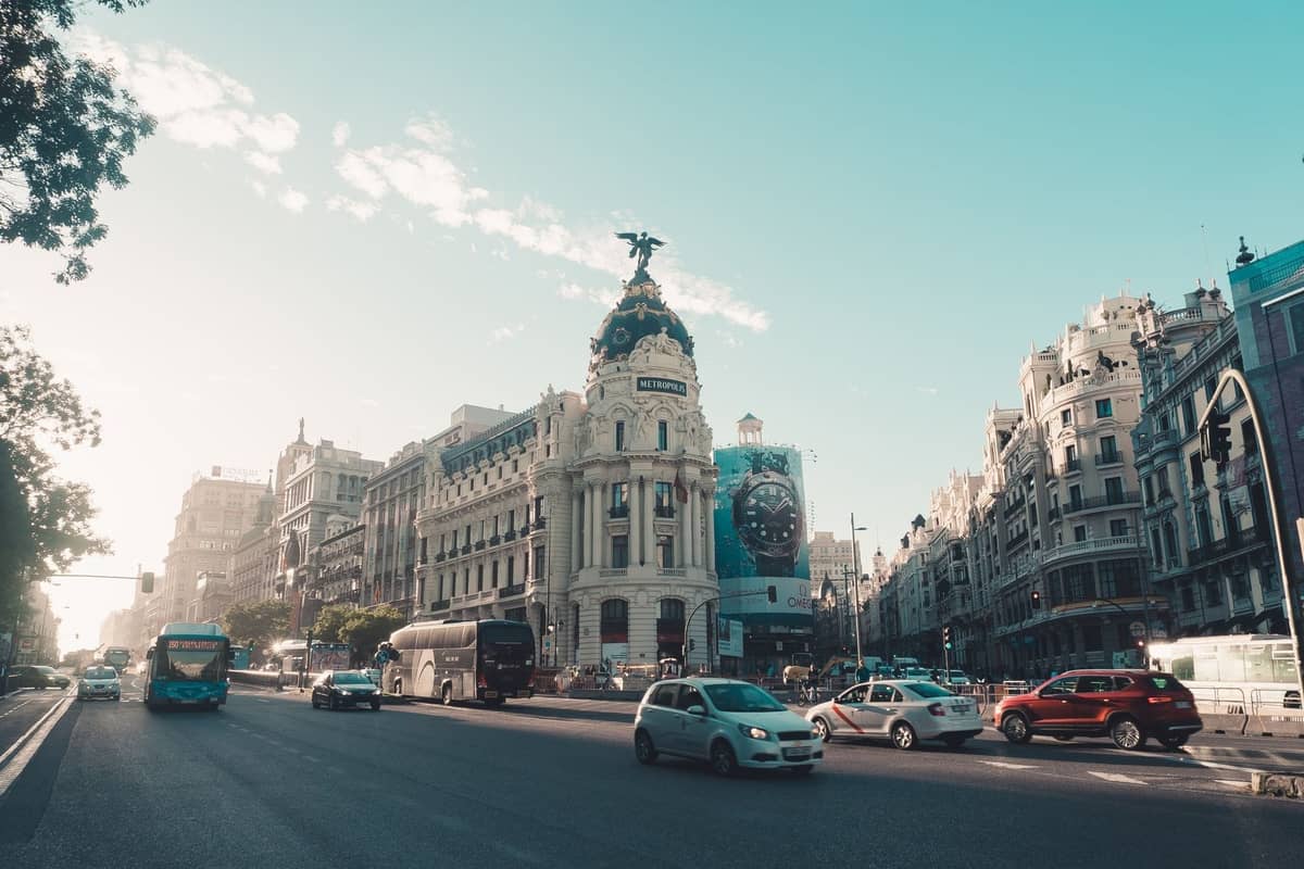 Ampia veduta della Gran Vía di Madrid con autobus urbani, auto e l'edificio Metrópolis sullo sfondo in una giornata di sole.