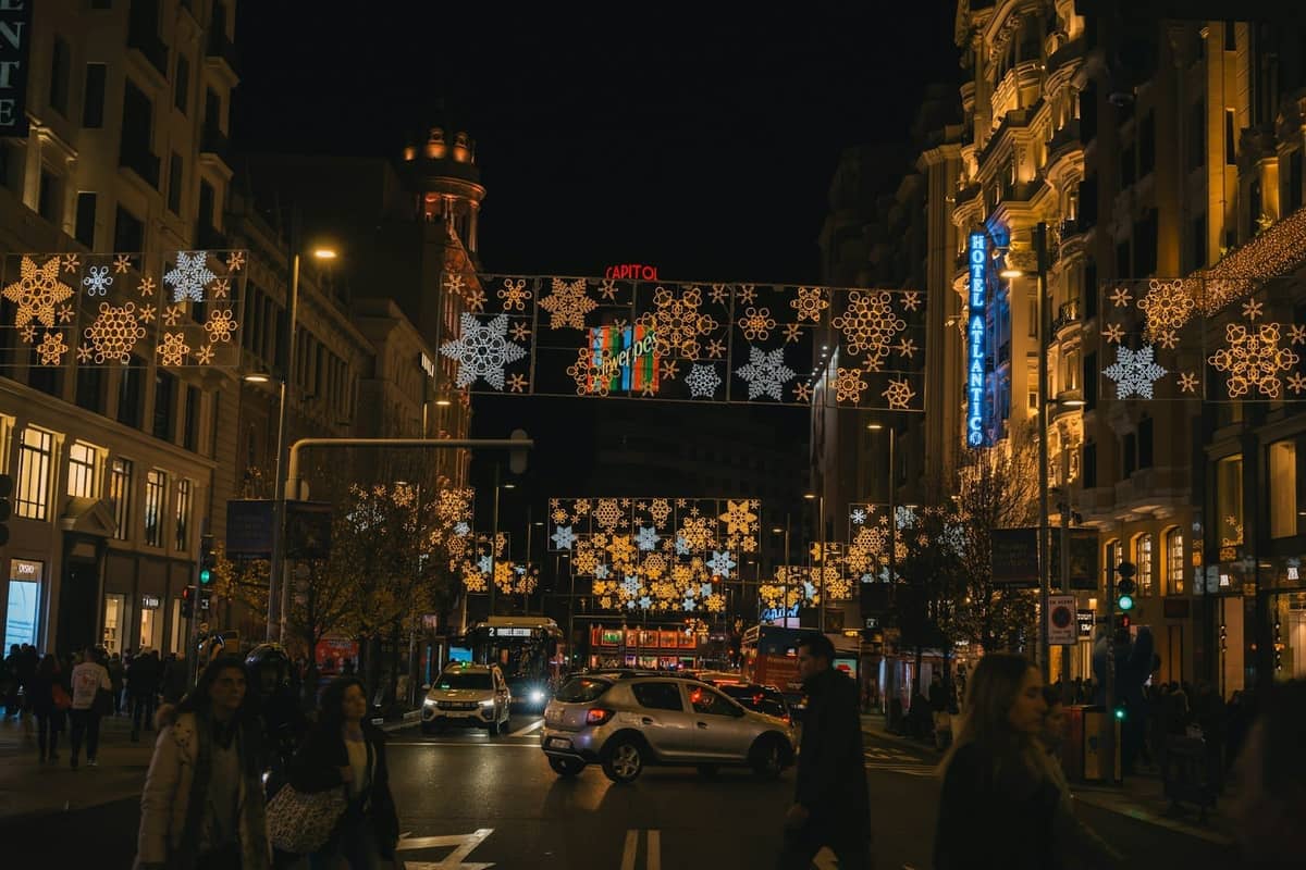 Nächtliche Szene auf der Gran Vía in Madrid mit festlichen Weihnachtslichtern über einer belebten Straße und Menschenmassen.