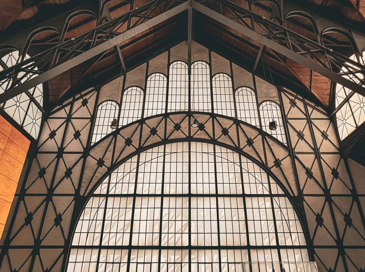 Architektonisches Innendetail einer historischen Markthalle aus Eisen und Glas, mit geometrischen Mustern und großen Fenstern.