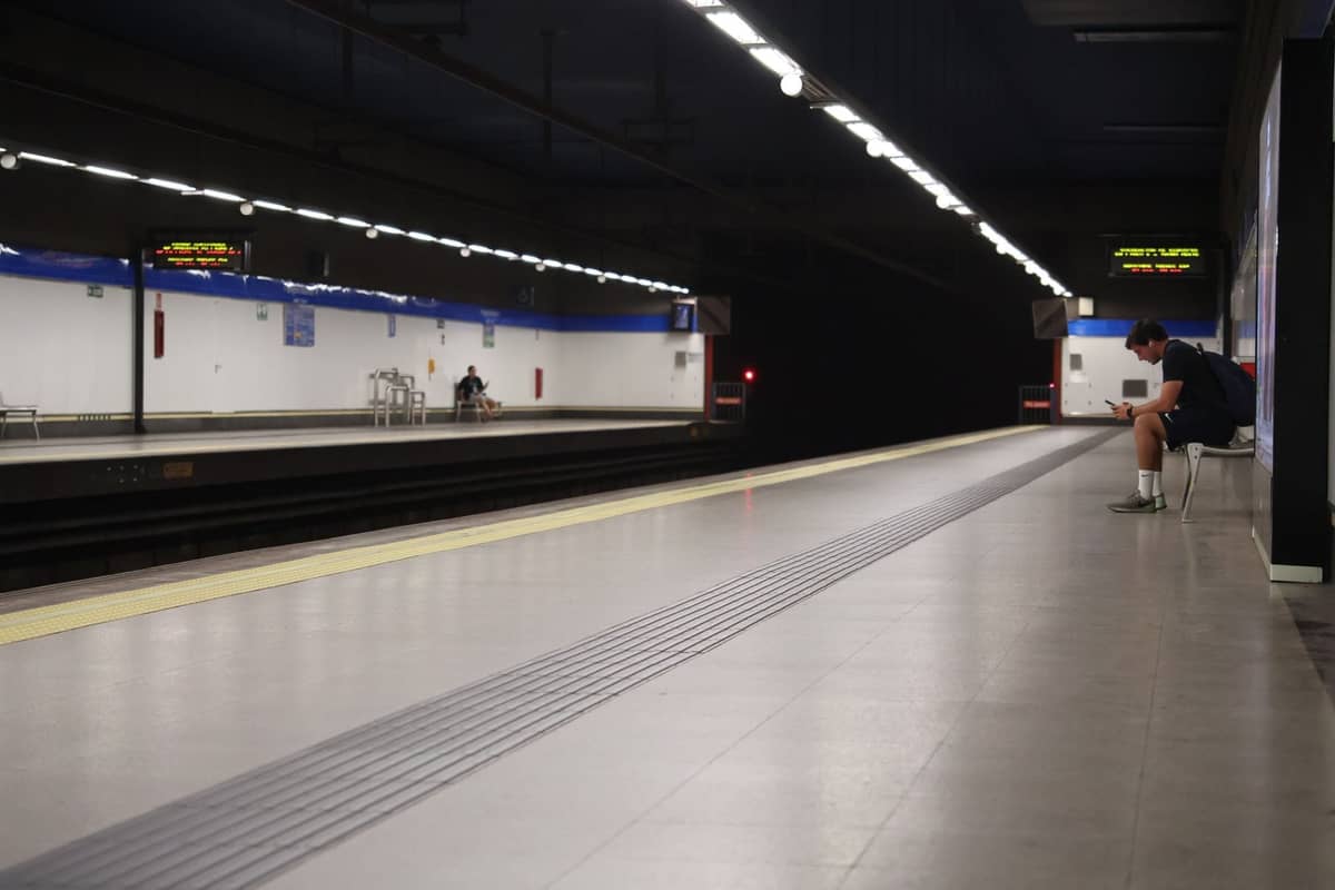 Puste nocne perony metra w Madrycie z jedną siedzącą osobą i jasnymi światłami sufitowymi.