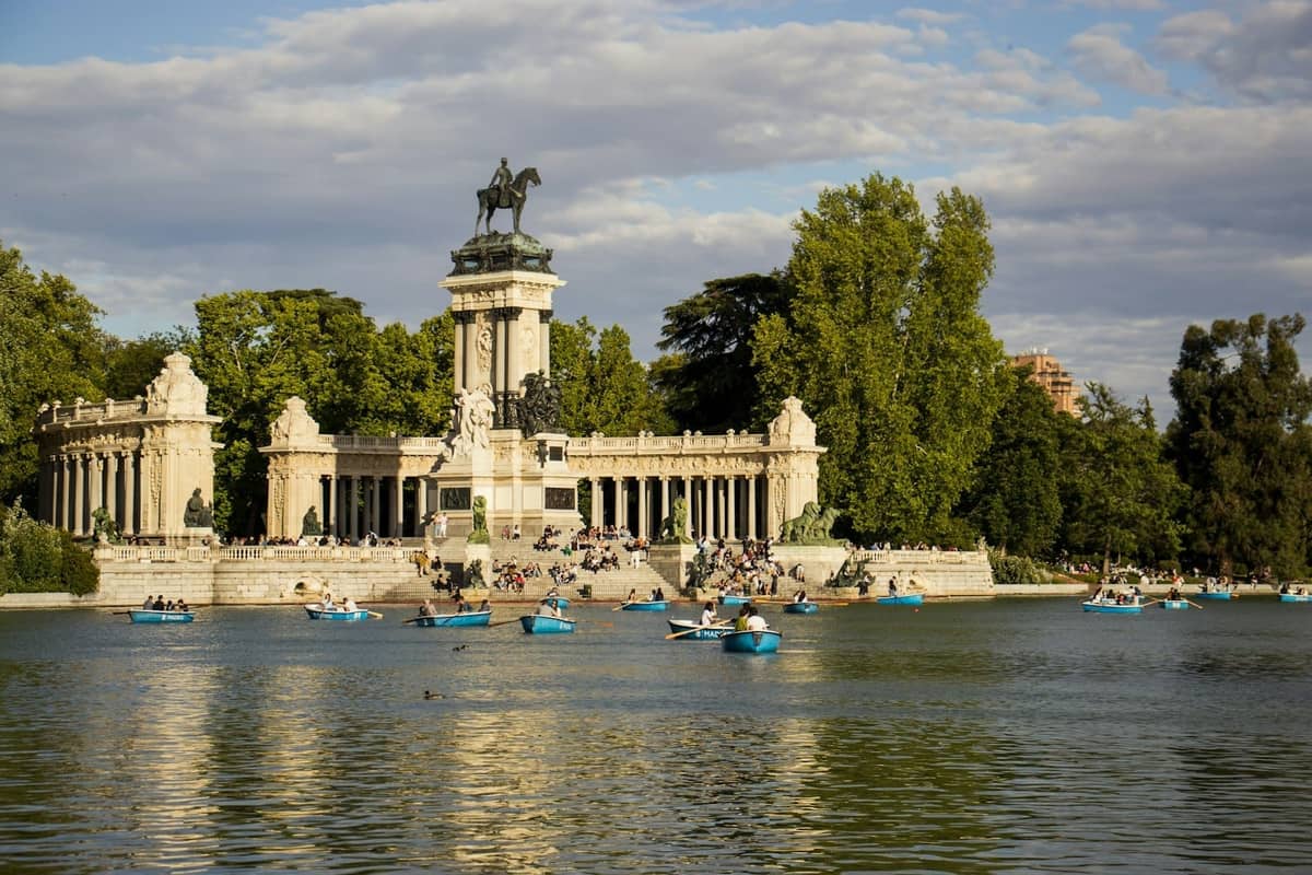 Madrid'deki El Retiro Parkı'nda güneşli bir günde Alfonso XII anıtının önündeki ana gölde tekne süren insanlar.