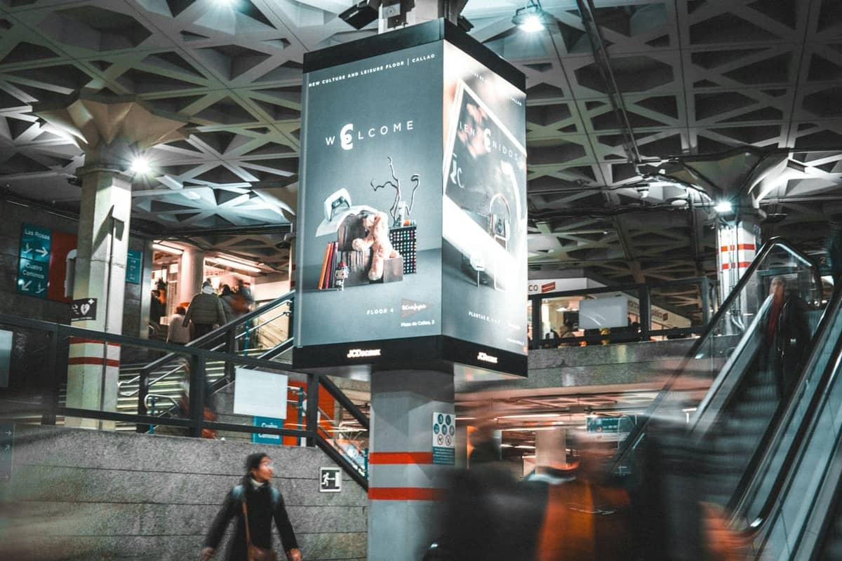 Intérieur animé d'une station de métro de Madrid avec des personnes qui marchent, des escalators et de grands panneaux en hauteur.