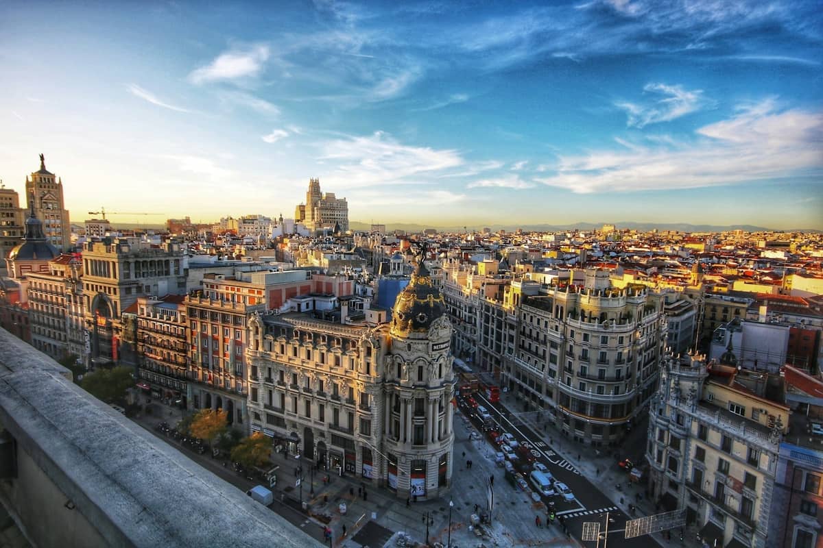 Vue aérienne panoramique de la Gran Via à Madrid avec son architecture classique, ses rues animées et la ligne d'horizon de la ville sous un ciel bleu clair.