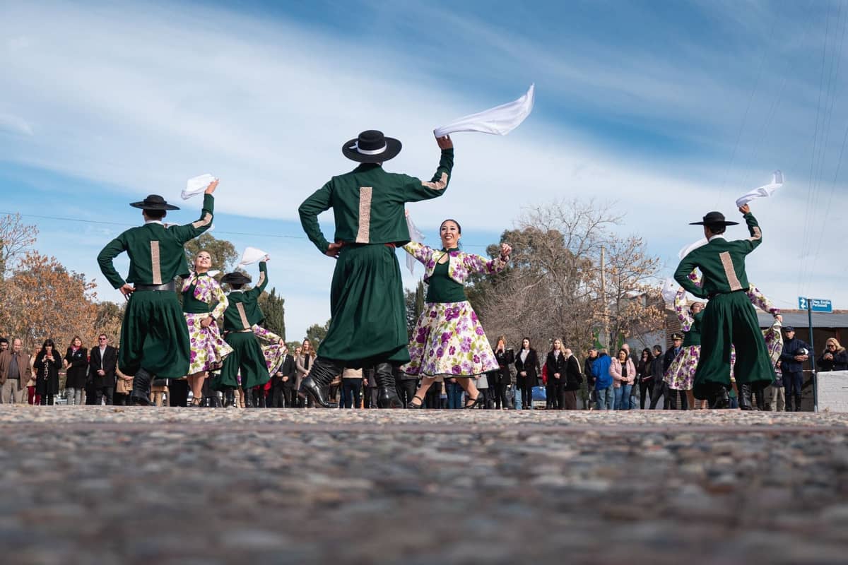 Gruppe von Tänzern in traditioneller spanischer Tracht, die auf einer Plaza im Freien auftreten, beobachtet von einer Menge unter blauem Himmel.