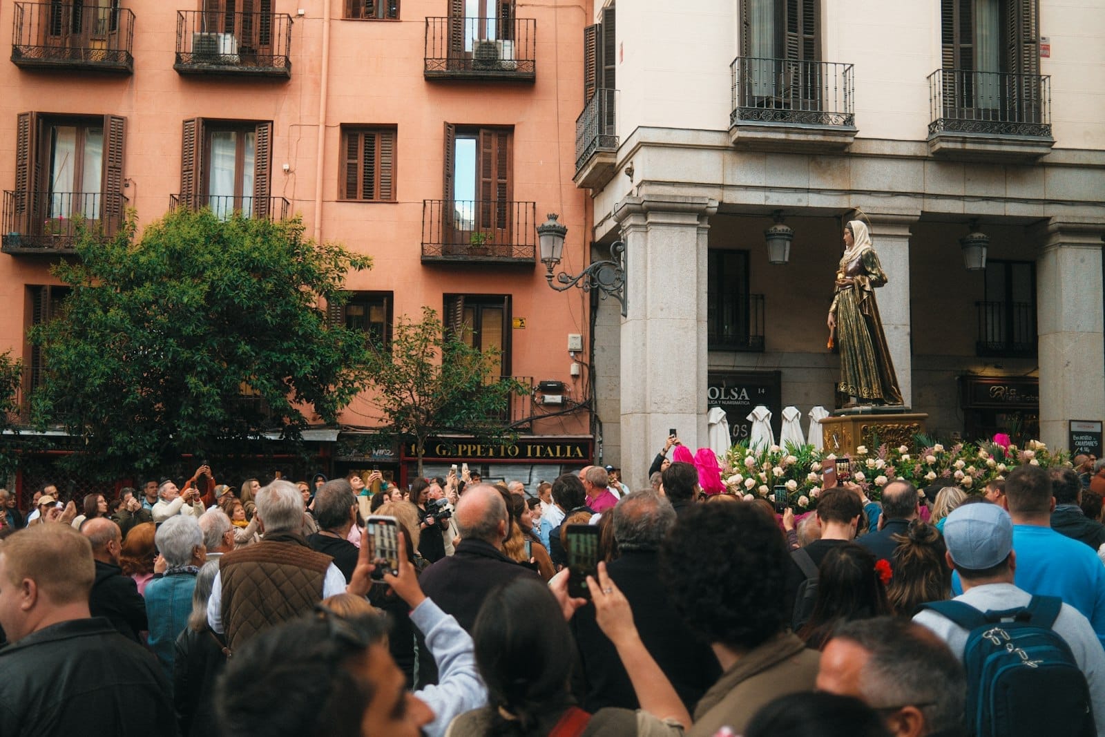 Grande multidão reunida em uma rua de Madrid assistindo a uma procissão religiosa com uma estátua de um santo cercada de flores durante o Festival de San Isidro.