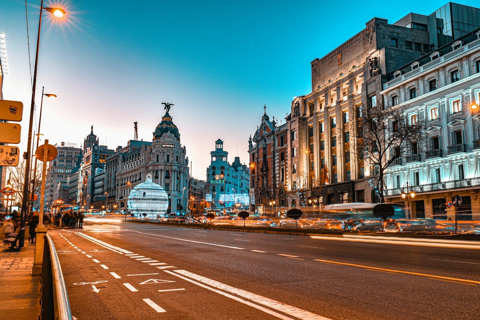 Vista vibrante da Gran Vía em Madri ao entardecer, com arquitetura icônica, trânsito intenso, vitrines iluminadas e uma atmosfera urbana animada.
