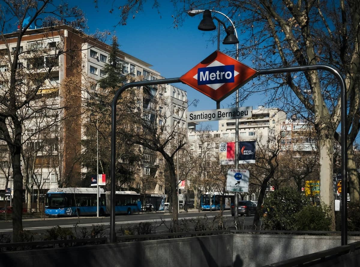 Açık bir günde arka planda şehir binaları ve otobüslerle Madrid Santiago Bernabéu metro istasyonunun girişi