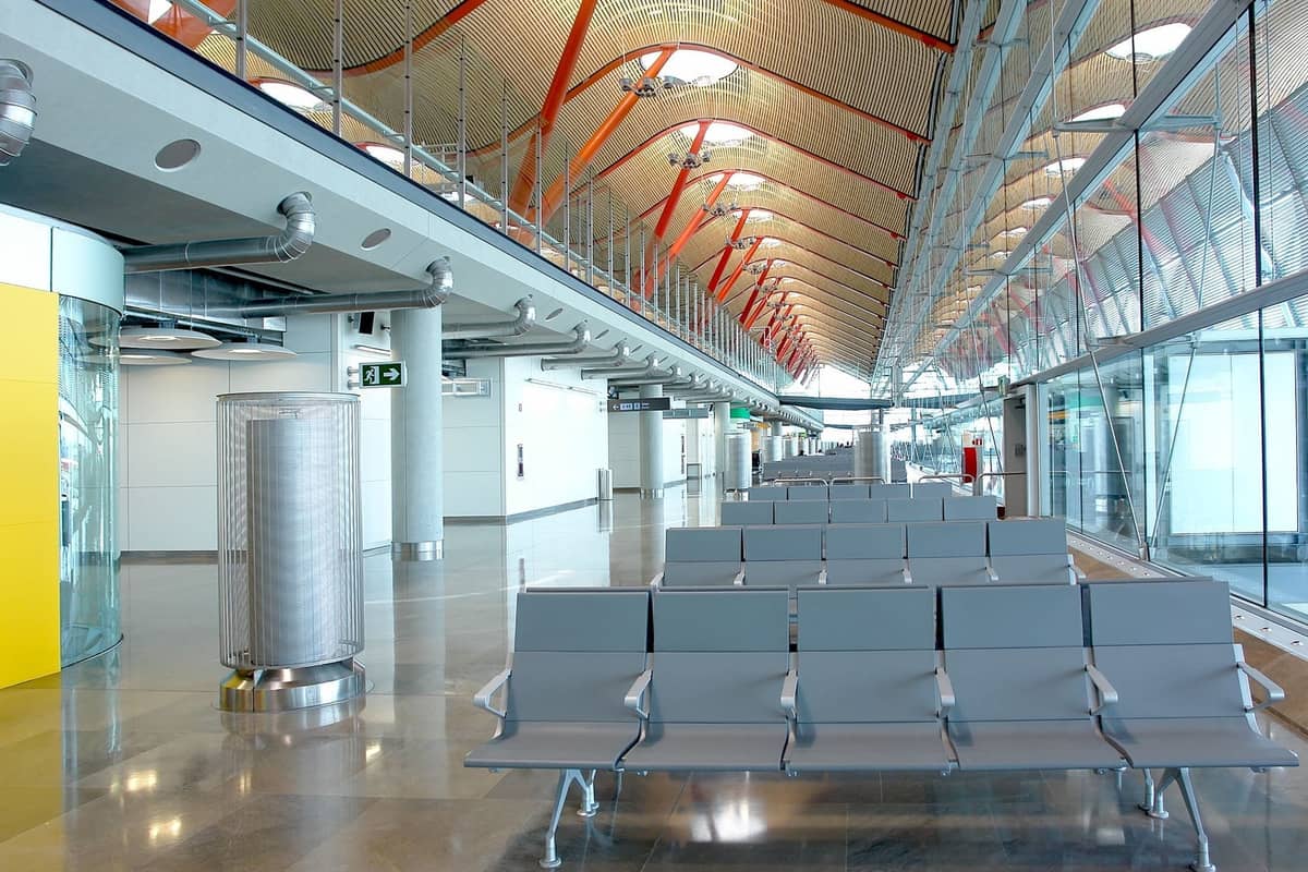 Sala de embarque moderna en el Aeropuerto Adolfo Suárez Madrid-Barajas con asientos vacíos, techo característico de madera y rojo, y paredes de cristal.
