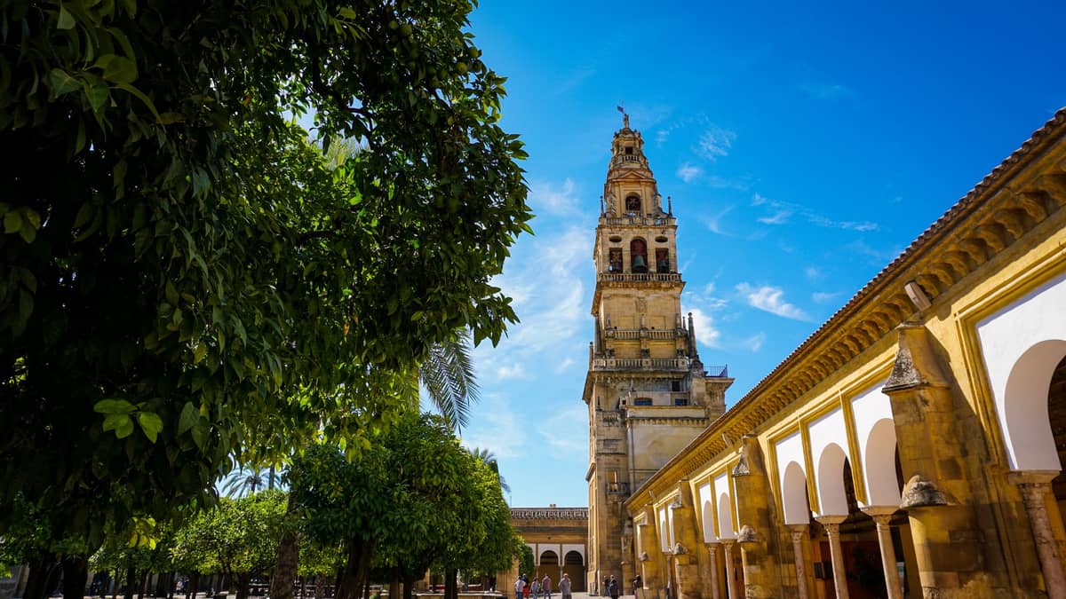 วิวภายนอกของหอระฆังและลานของ Mezquita-Catedral ในเมือง Córdoba ในวันที่แดดสดใสท้องฟ้าสีฟ้าและต้นไม้สีเขียว