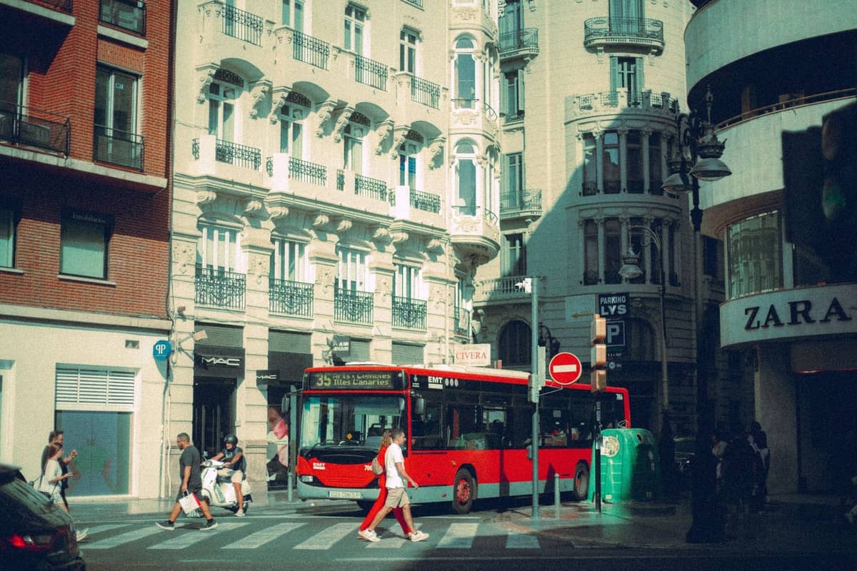 Ein roter Stadtbus fährt durch eine Kreuzung im Zentrum von Madrid mit historischen Gebäuden und Fußgängern in der Nähe.