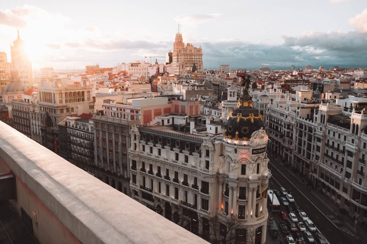 Luftaufnahme der Gran Vía in Madrid mit dem ikonischen Metropolis-Gebäude im Sonnenlicht und der Stadtlandschaft bis zum Horizont.