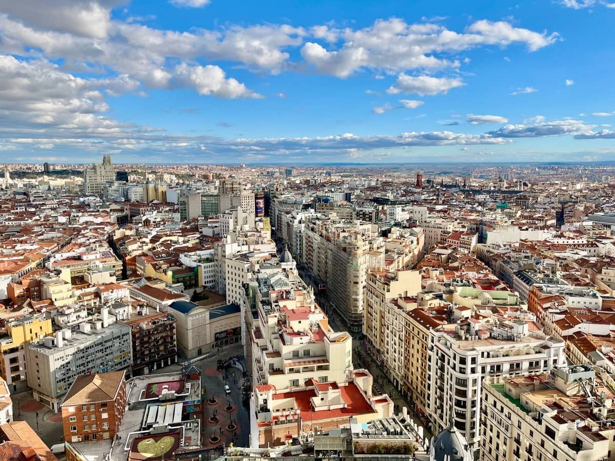 Ampia vista aerea di Madrid che mostra il paesaggio urbano con edifici fitti e l'orizzonte sotto un cielo azzurro brillante con nuvole sparse.
