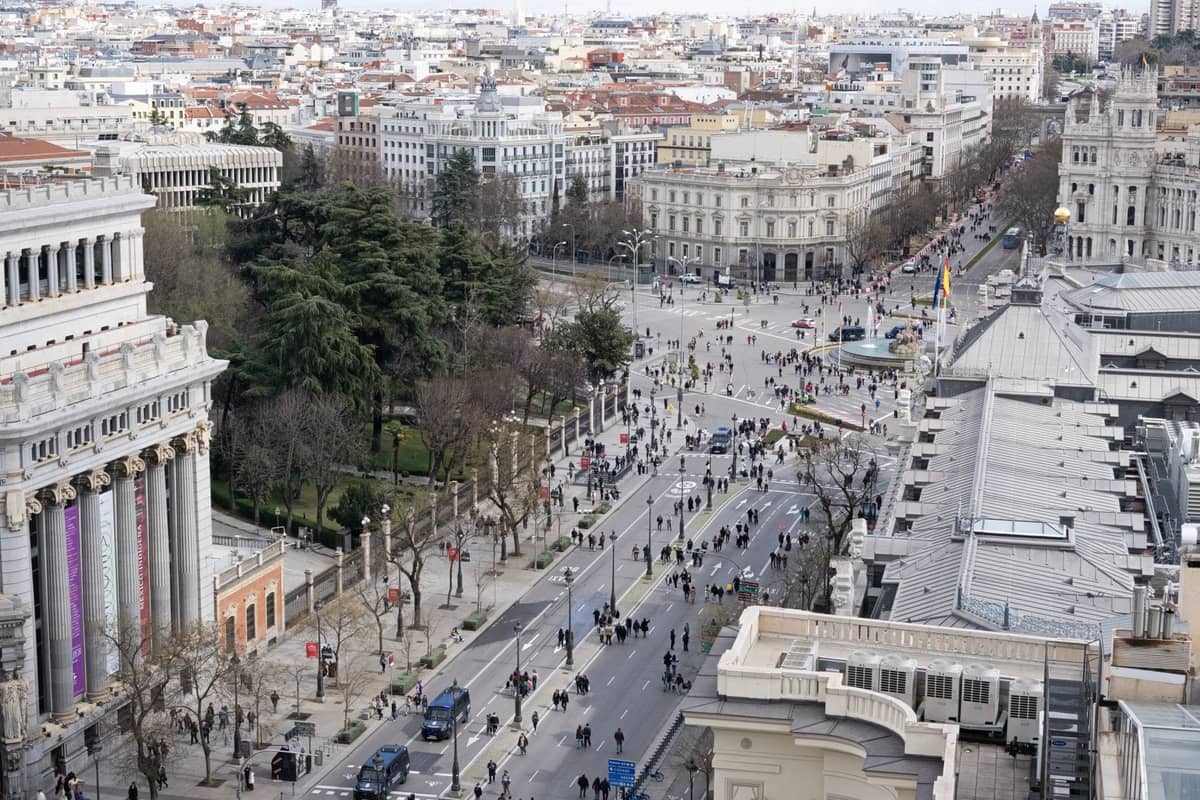 Luftaufnahme des Zentrums von Madrid mit großen Boulevards, Menschen auf breiten Straßen, historischen Gebäuden und sichtbaren Grünflächen.