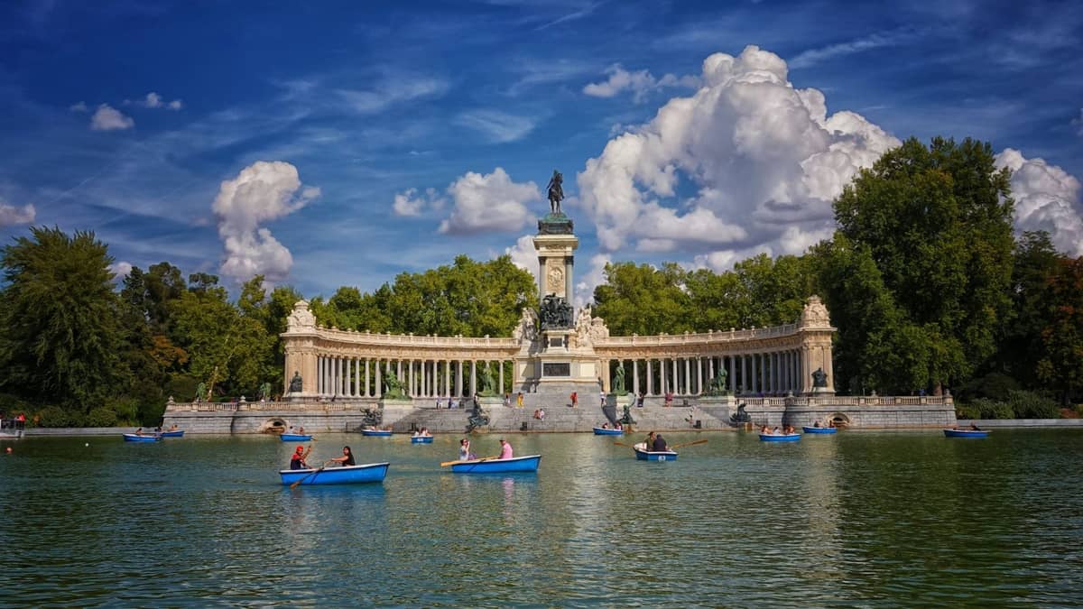 Barche a remi con famiglie e bambini sul grande lago centrale di fronte al monumento Alfonso XII, Parque del Retiro, Madrid, in una giornata di sole