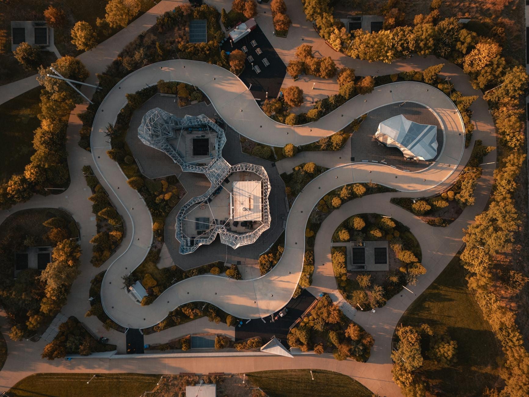 Vista aerea del Maggie Daley Park con sentieri pavimentati sinuosi, strutture geometriche per il gioco, lussureggianti alberi verdi e luce dorata del sole sui giardini paesaggistici.