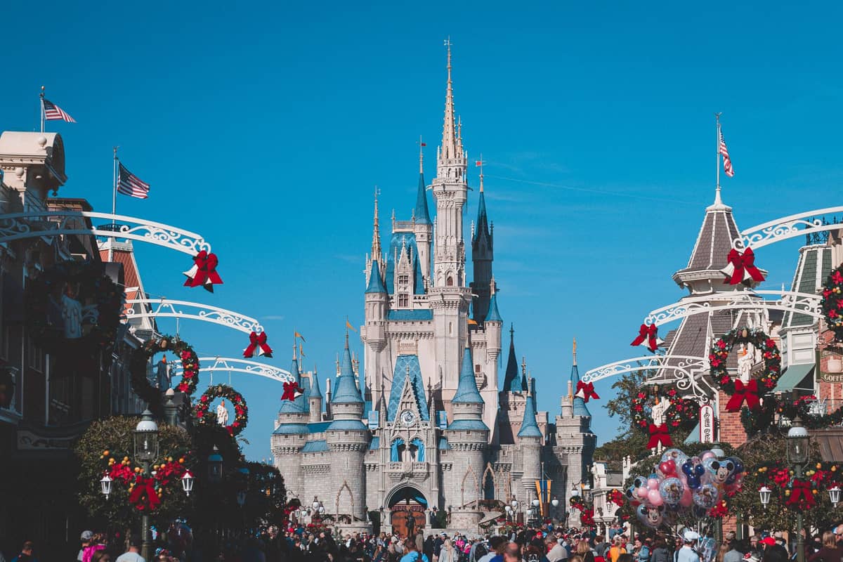 Cinderella Castle at Magic Kingdom Park on a clear sunny day, surrounded by festive Main Street decorations and large crowds of visitors.