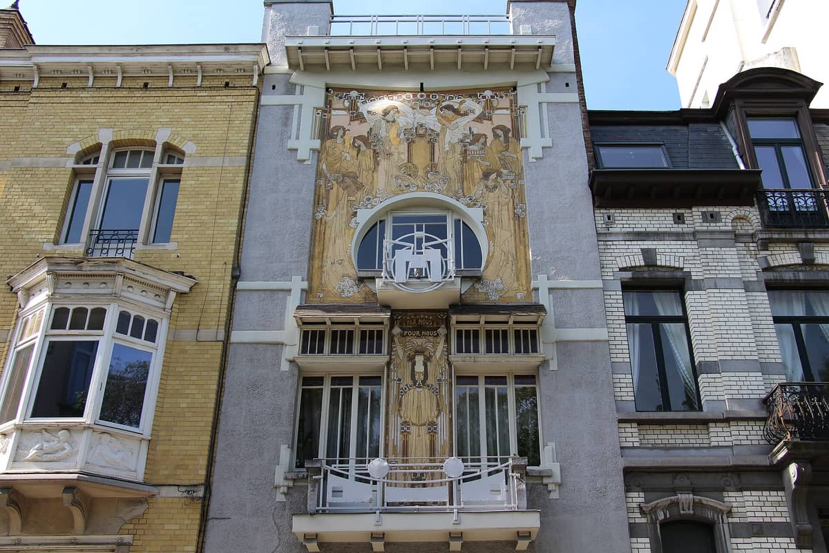 Fachada frontal da Maison Cauchie em Bruxelas, com seus intrincados murais Art Nouveau e detalhes arquitetônicos únicos entre as casas vizinhas.