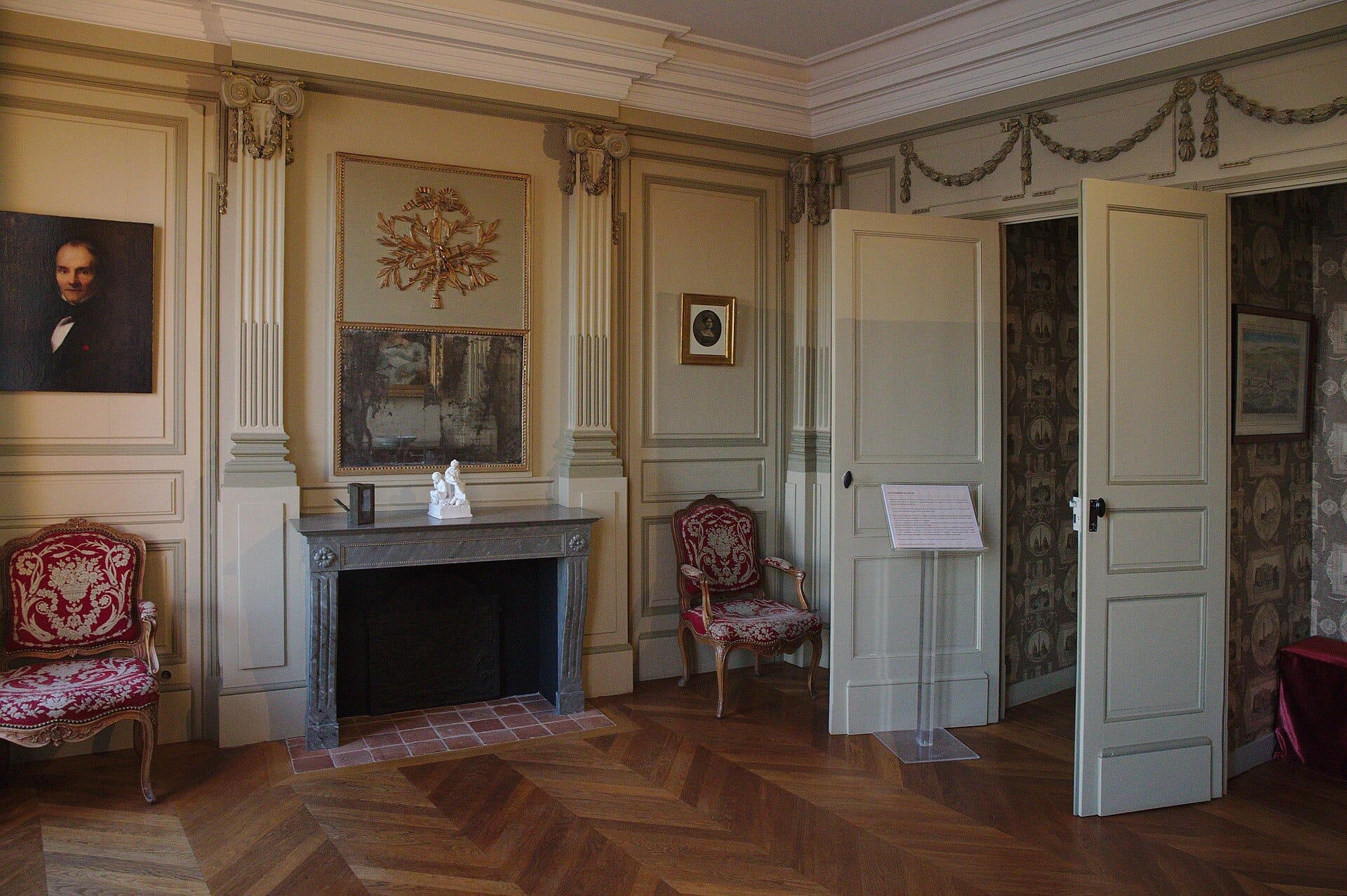 Elegante interno settecentesco della Maison de l'Armateur con pannelli murali ornati, un camino in marmo, sedie tappezzate in rosso e opere d'arte classiche.
