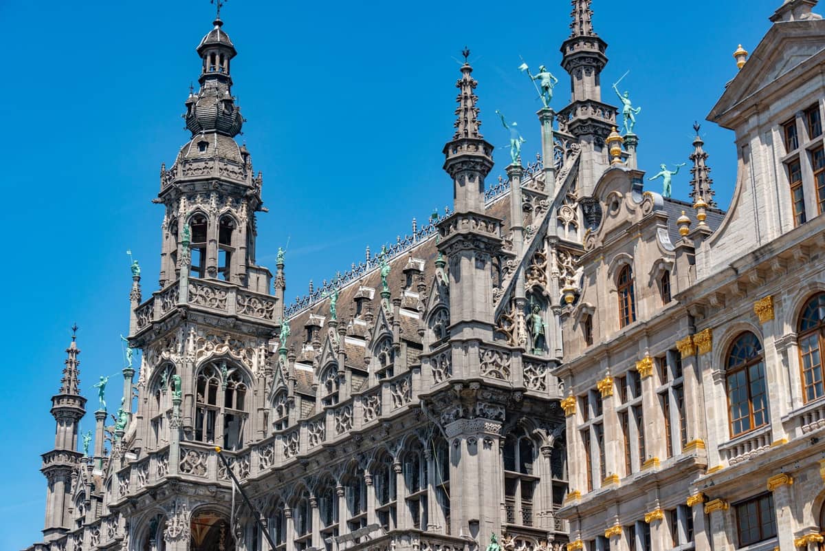 Fachada gótica ornamentada da Maison du Roi com torres e estátuas sob um céu azul intenso, na Grand-Place de Bruxelas.