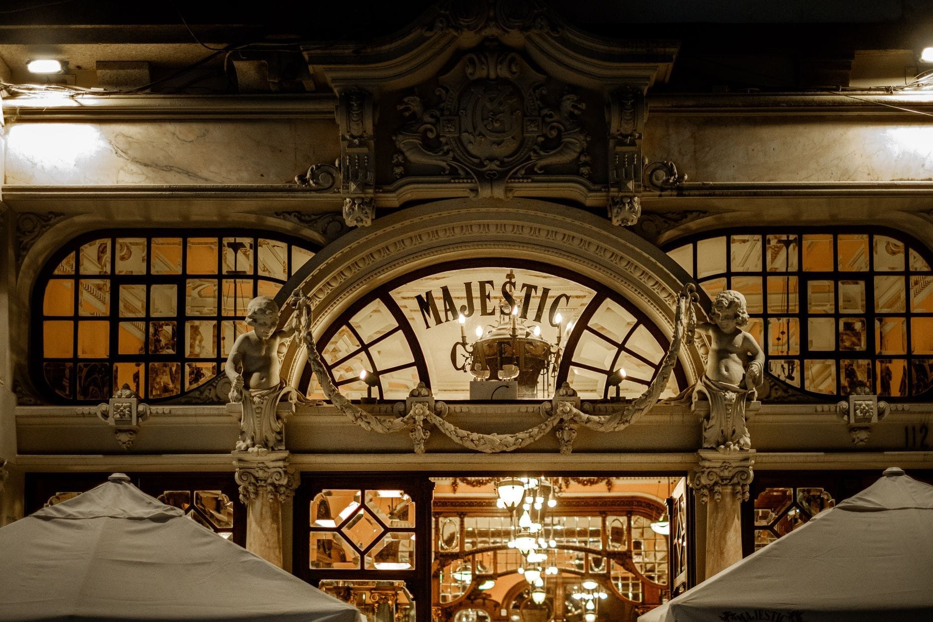 La sontuosa facciata del Café Majestic a Porto, con cherubini scolpiti, grandi archi e specchi calorosamente illuminati che riflettono l'interno Belle Époque del caffè.