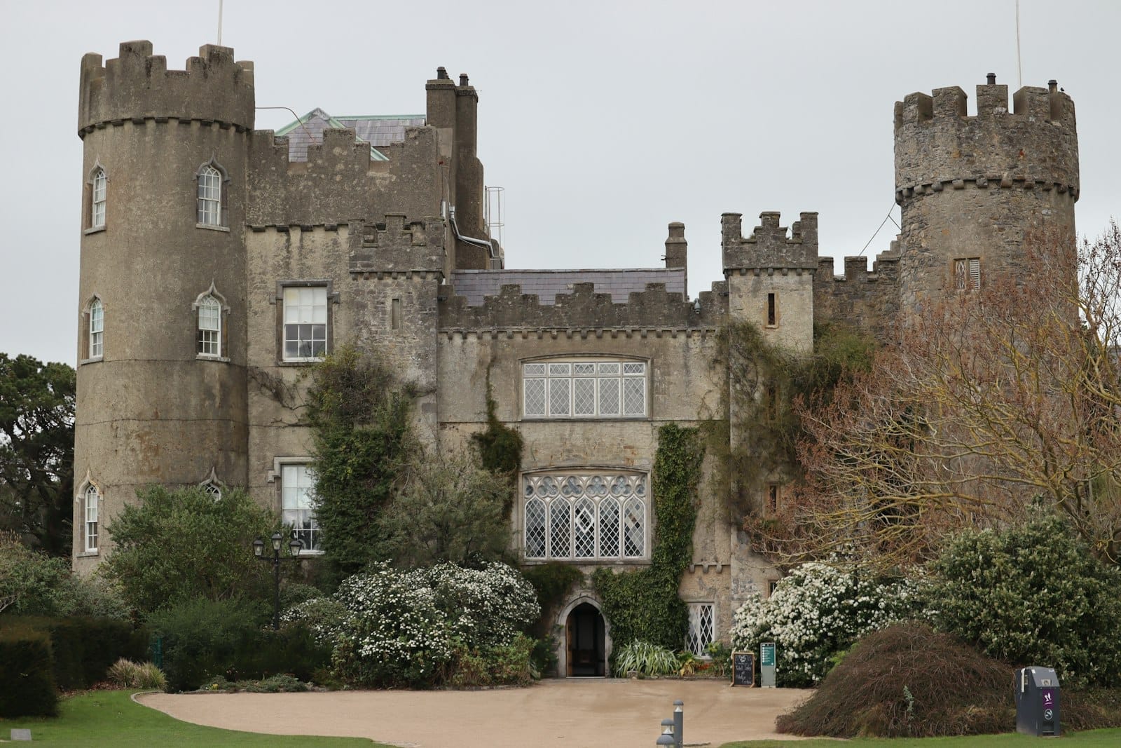 Vista frontale del Castello di Malahide con le sue iconiche torri rotonde, la facciata in pietra medievale, l'ingresso ad arco e i rigogliosi giardini circostanti in fiore in primavera.