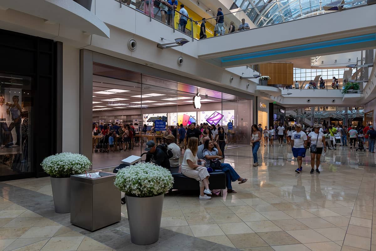 Innenansicht des Mall at Millenia mit Apple Store, Einkaufenden, Sitzbereichen und zwei Etagen unter einem lichtdurchfluteten Atrium.