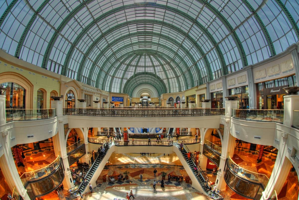 Weitläufige Innenansicht der Mall of the Emirates mit dem markanten Bogenglasdach, mehreren Einkaufsebenen, Rolltreppen und bummelnden Besuchern.