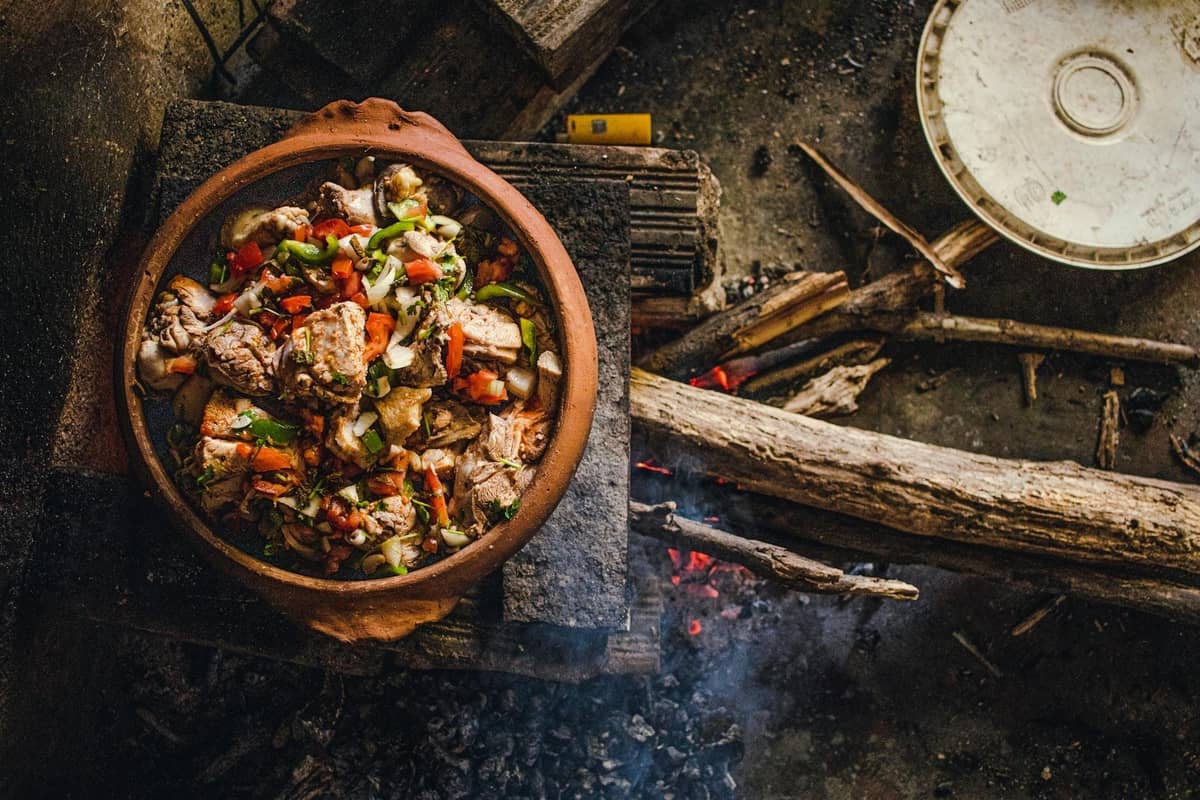 Ein rustikaler Tontopf gefüllt mit herzhaftem Fleisch und Gemüse, das über einem Holzfeuer köchelt, und die traditionelle bäuerliche Küche Mallorcas heraufbeschwört.
