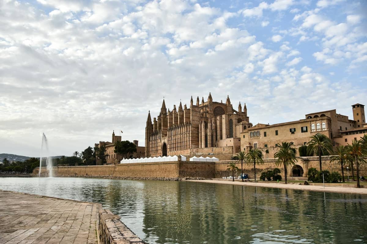Tanawin ng Katedral ng Palma sa tabi ng isang replektibong pool sa ilalim ng bahagyang maulap na langit, na naglalarawan ng mahinahong panahon ng taglagas sa Mallorca.