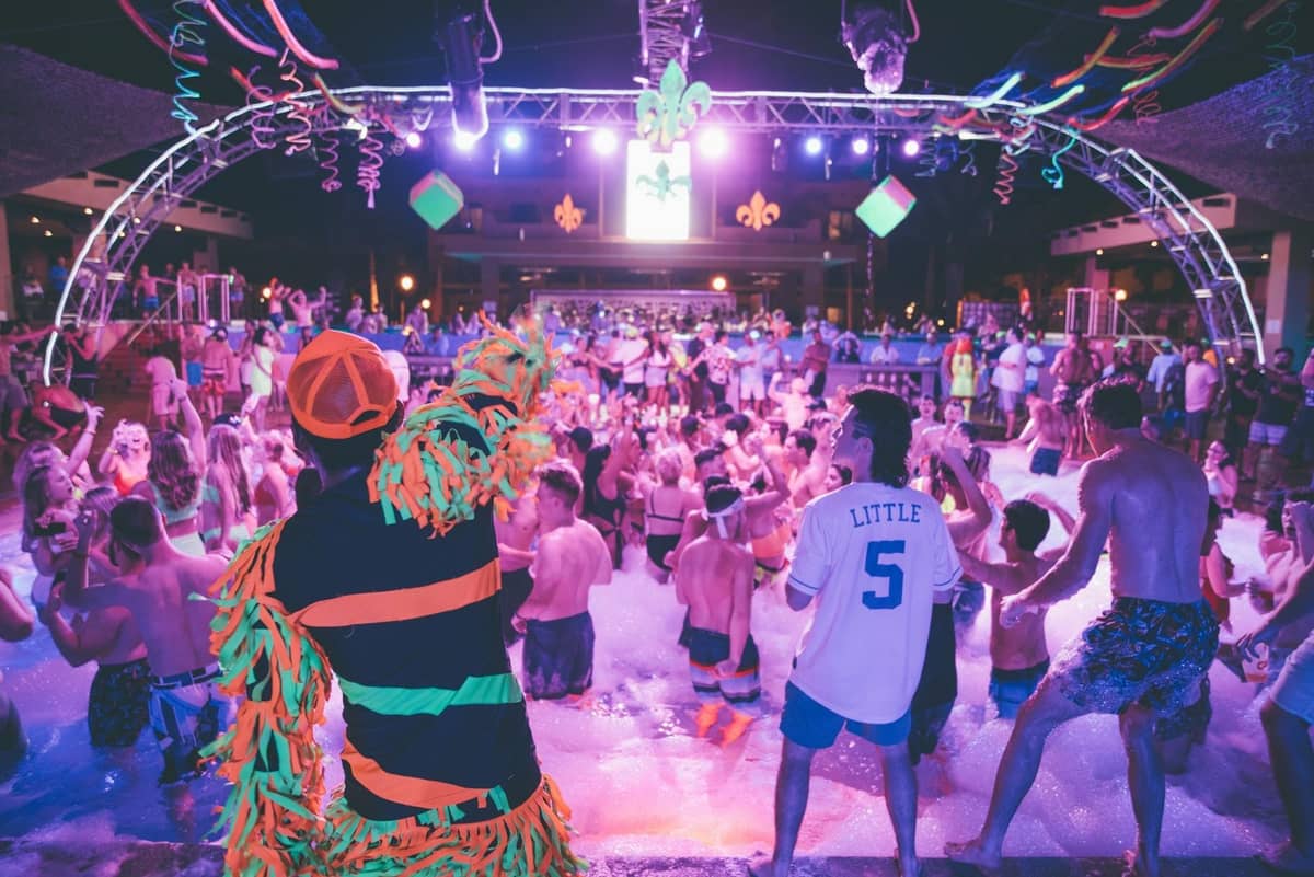 Gran multitud en una fiesta de espuma nocturna al aire libre con luces de escenario coloridas y un ambiente animado típico de los clubes de los resorts mediterráneos.