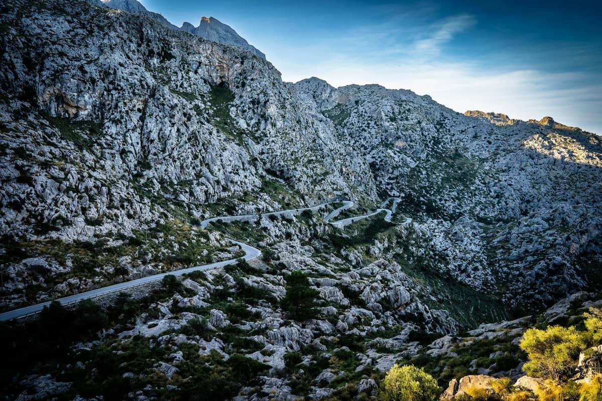 Una tortuosa strada di montagna si snoda tra scogliere rocciose e un terreno accidentato, raffigurando le drammatiche curve del Sa Calobra Loop a Maiorca.