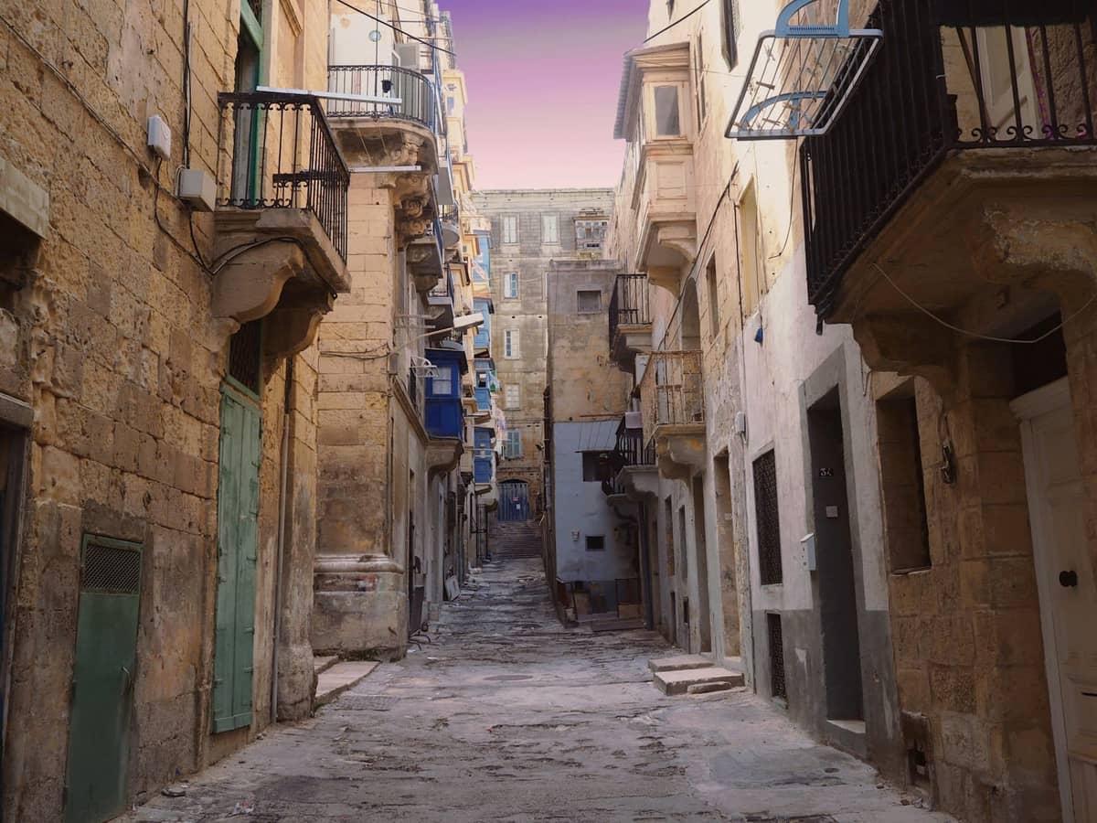 Mga gusaling bato at makipot na kalye sa Valletta, Malta sa takipsilim, na nagpapakita ng mga balkonahe at katangiang arkitekturang Maltese.