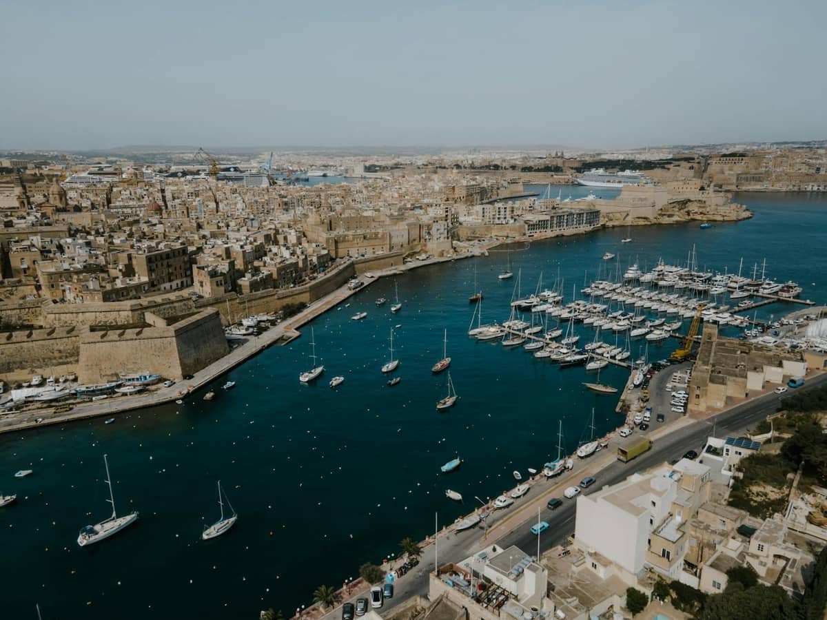 Вид с воздуха на Grand Harbour на Мальте с историческими укреплениями, марина со множеством яхт и золотистыми городскими зданиями.