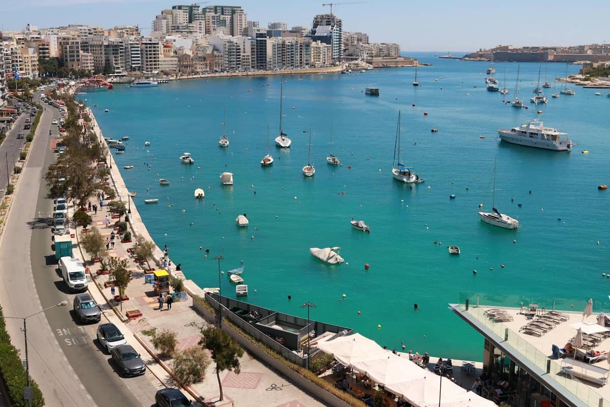 Aerial view of Sliema waterfront in Malta with boats in a turquoise bay, modern buildings, and busy coastal road—prime area for divers’ logistics.