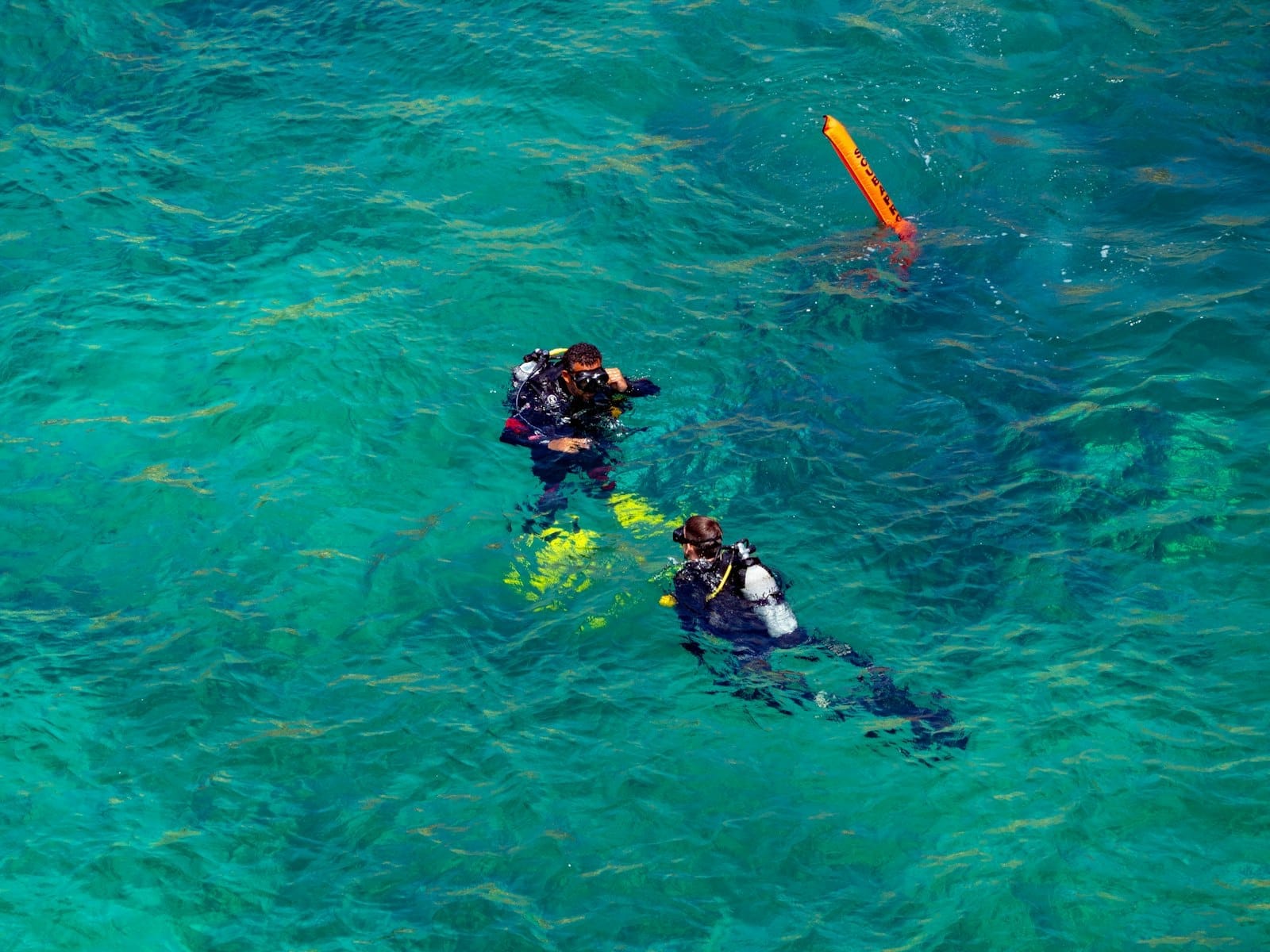 Dois mergulhadores flutuando em água turquesa e cristalina do Mediterrâneo perto de Malta, se preparando para mergulhar com equipamentos visíveis, transmitindo uma sensação de aventura.