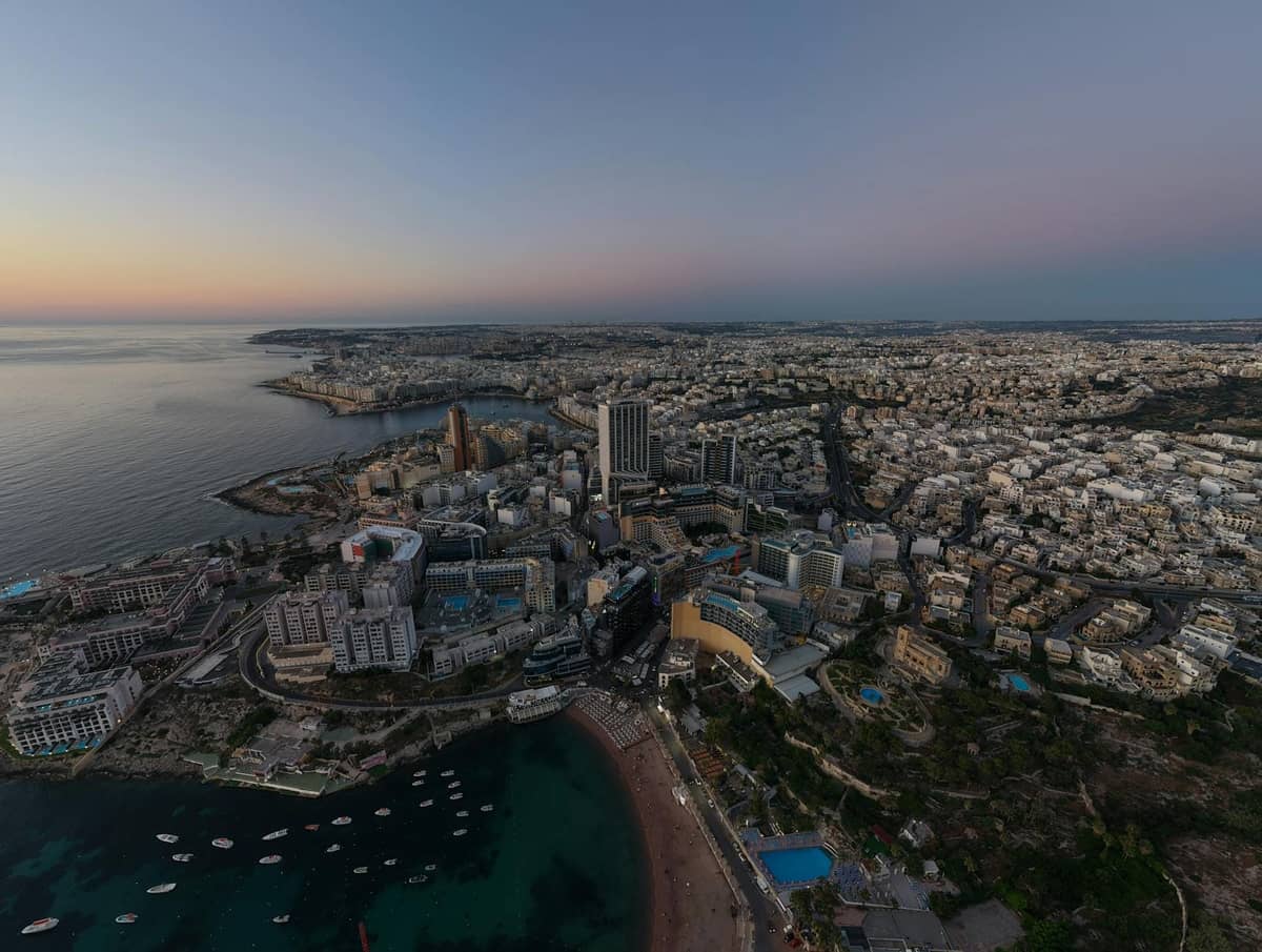 Cảnh nhìn từ trên cao của bờ biển Malta với các tòa nhà dày đặc, khách sạn cao tầng và khu vui chơi về đêm gần bãi biển, chụp lúc hoàng hôn.