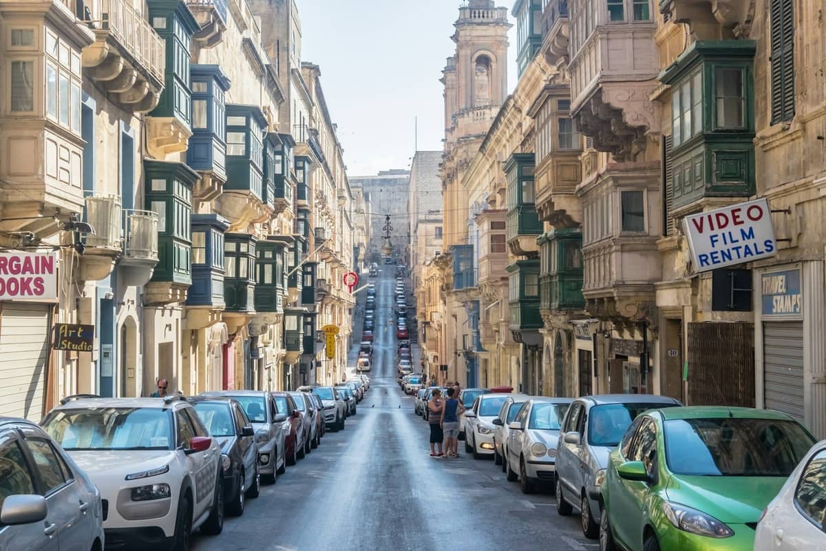 Enge Straße in Malta, gesäumt von dicht geparkten Autos und historischen Gebäuden, zeigt typische städtische Straßenverhältnisse.