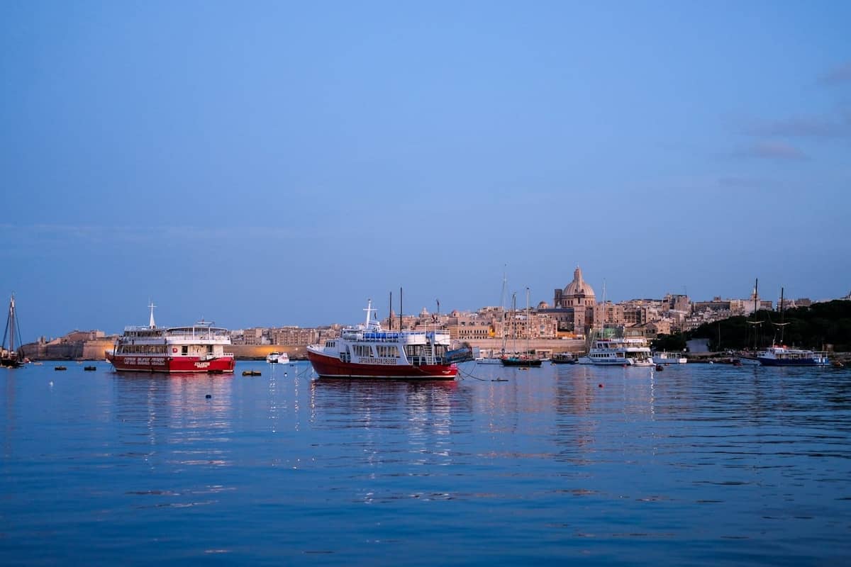 Ferries rojos y blancos en el puerto de Marsamxett con el horizonte de Valletta al fondo al atardecer en Malta.