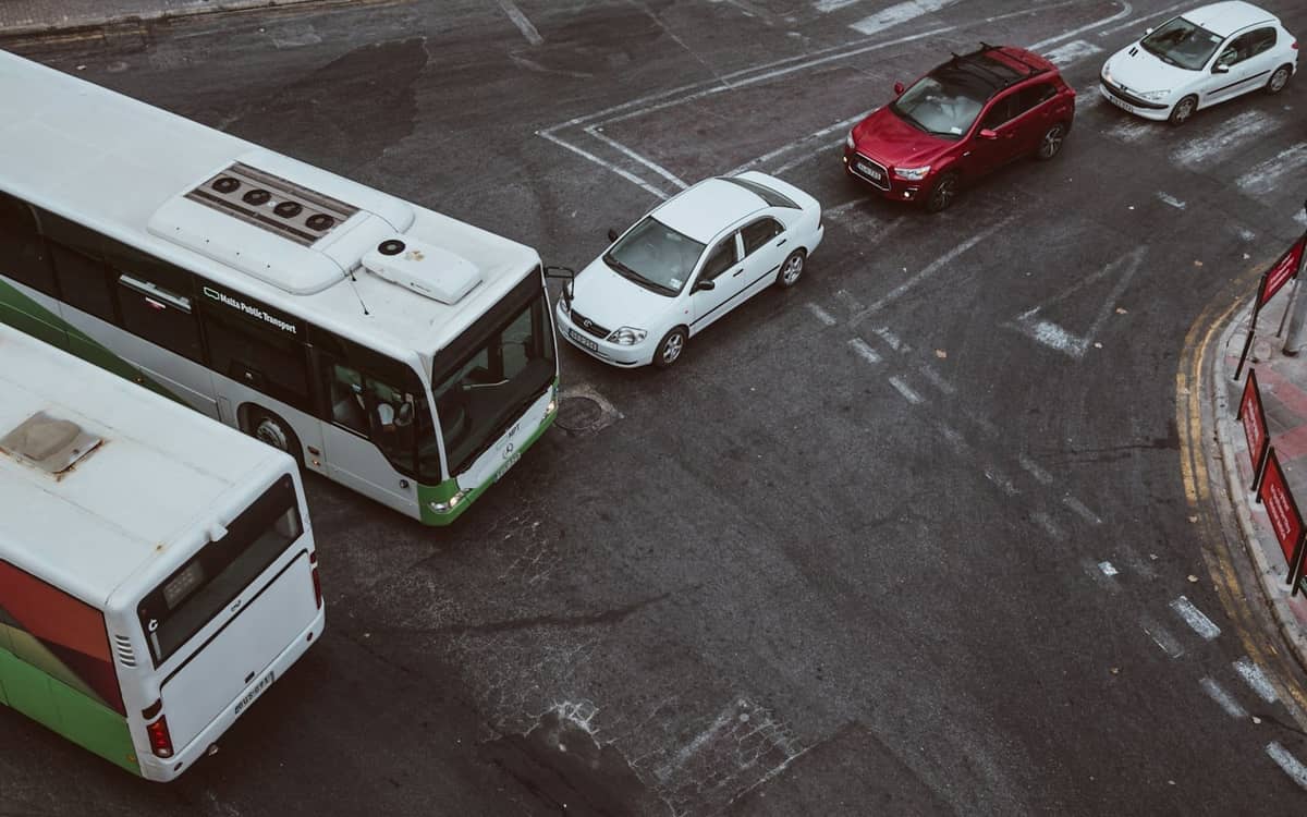 Autobus publiczny i kilka samochodów zatrzymanych na skrzyżowaniu na miejskiej ulicy Malty z widocznymi oznaczeniami drogowymi.