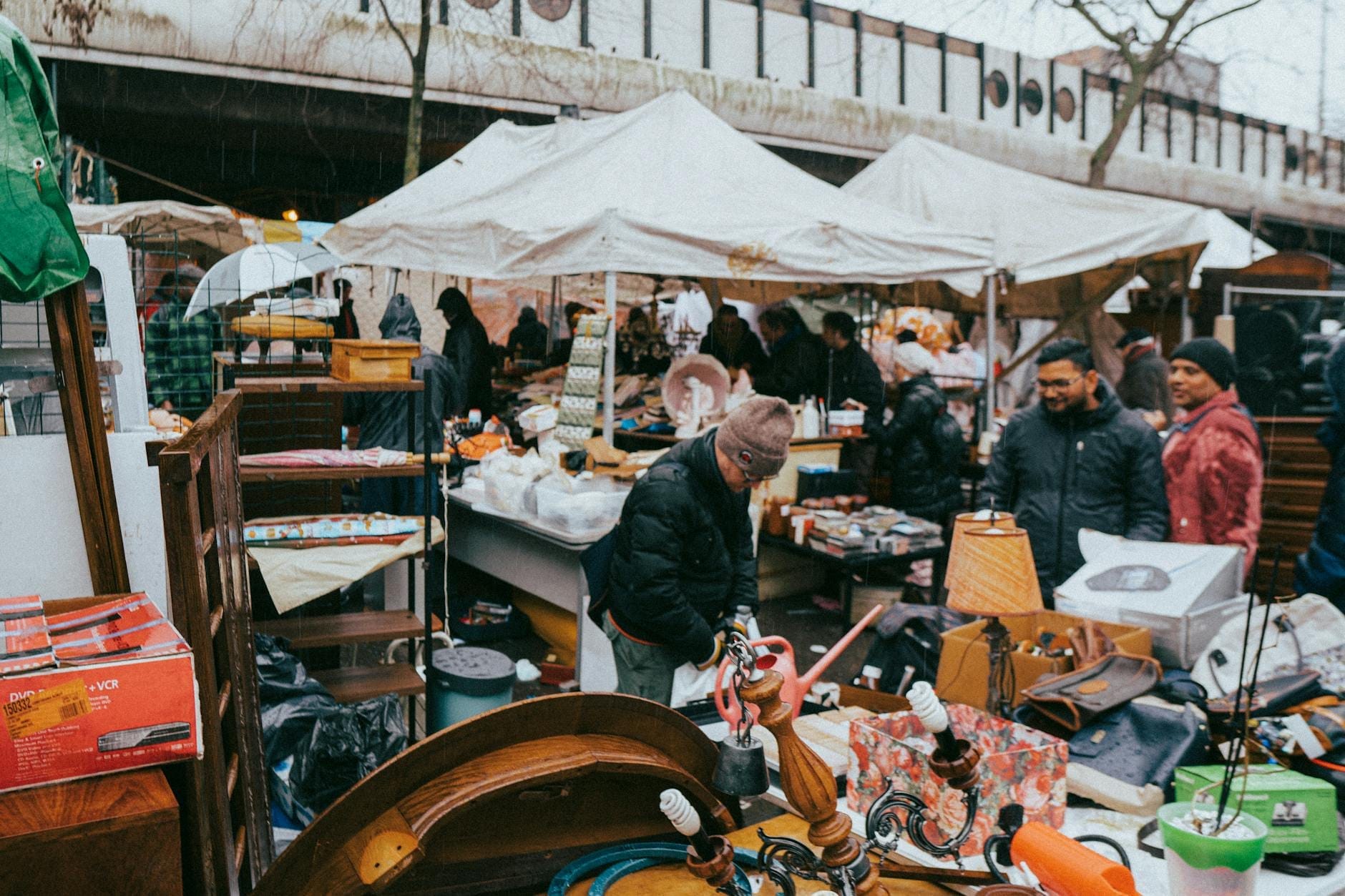 Mercato delle pulci all'aperto animato, con persone che curiosano tra le bancarelle sotto tende bianche piene di oggetti vintage, in una giornata nuvolosa a Parigi.