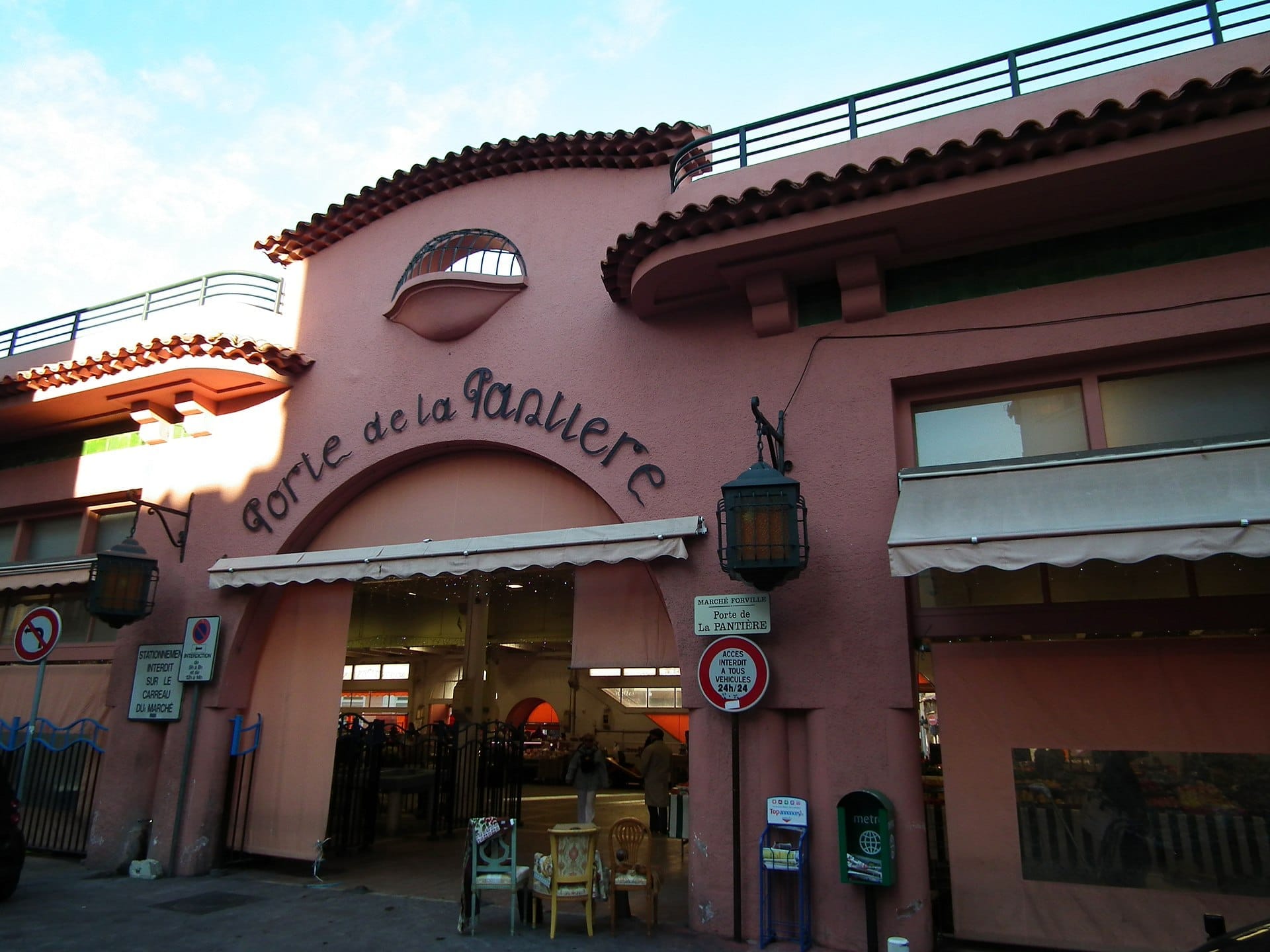 L'ingresso in stucco rosa del Marché Forville a Cannes, con scritte ad arco, lanterne e uno scorcio invitante dell'interno animato del mercato.