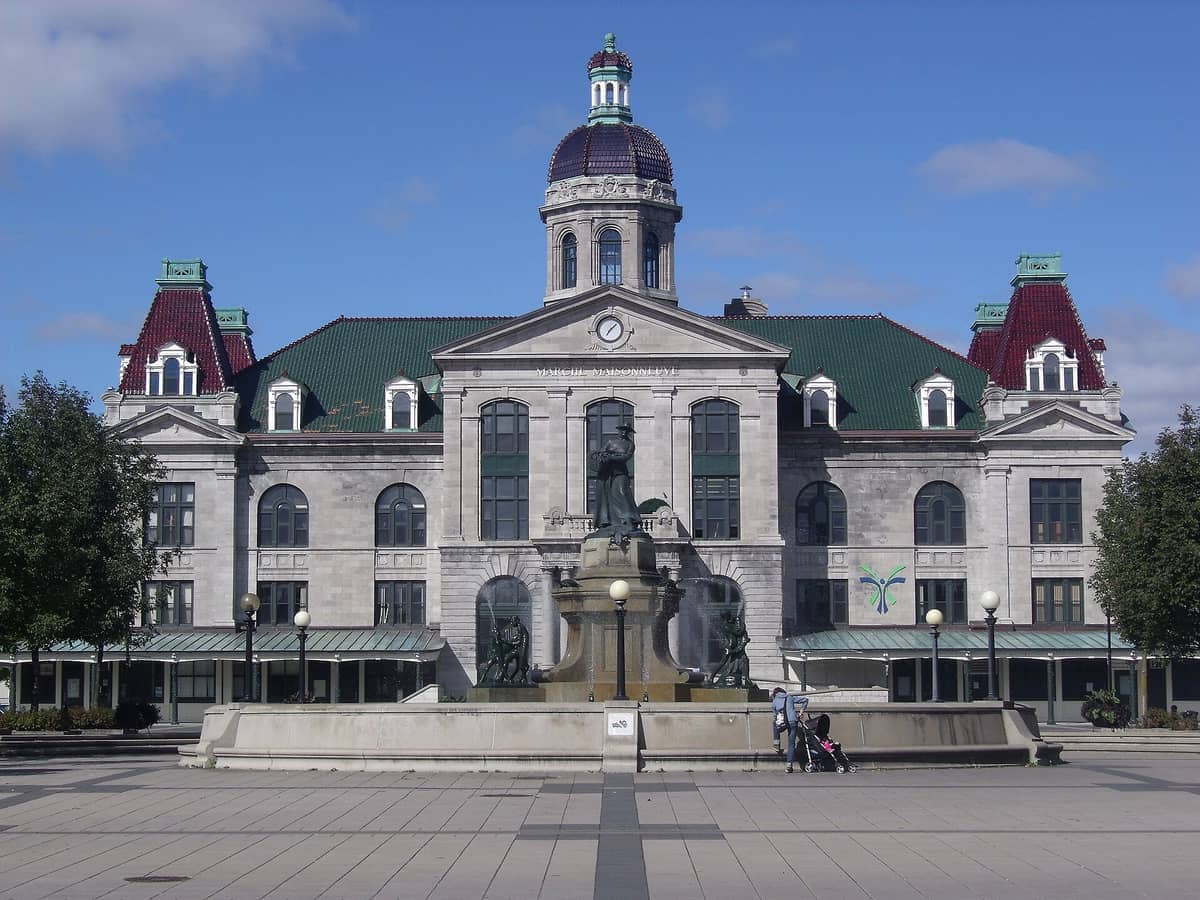 Historisches Gebäude des Marché Maisonneuve mit grünen und roten Dächern, zentraler Kuppel, Brunnen und klarem blauen Himmel im Osten Montréals.
