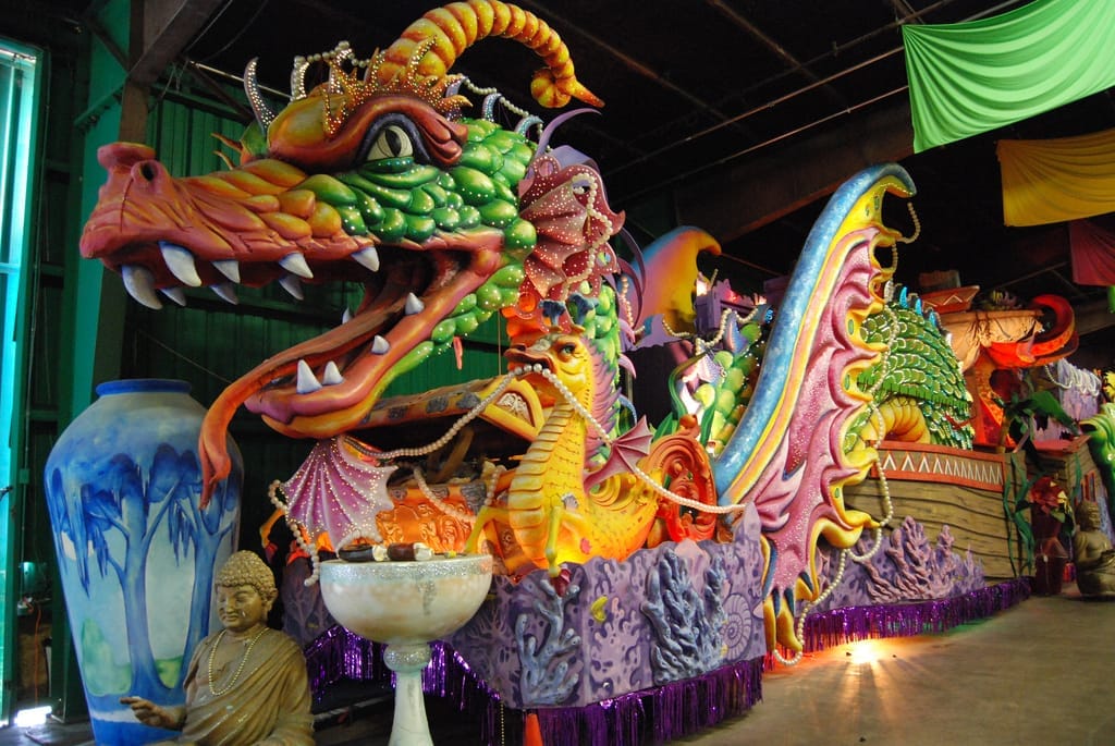 Enorme carro allegorico a tema drago colorato in costruzione al Mardi Gras World, circondato da decorazioni vivaci e sculture all'interno di un ampio magazzino.
