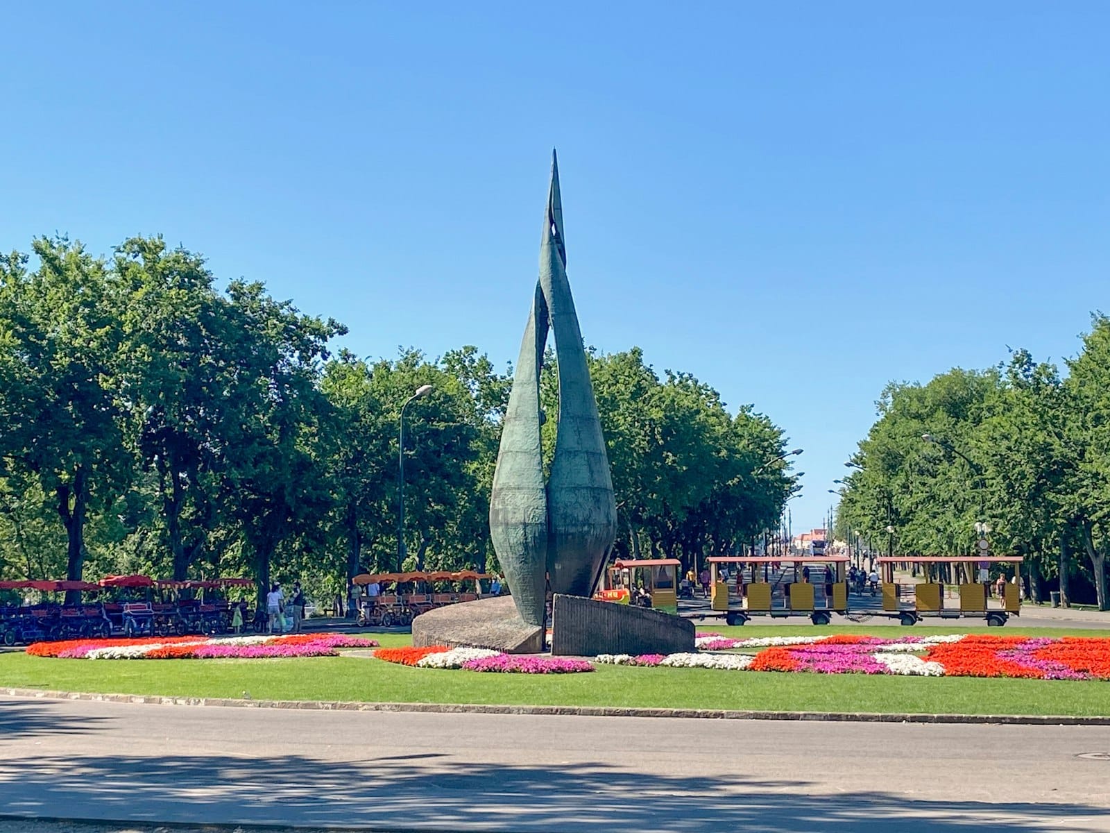 Giardino fiorito centrale con una scultura moderna alta, alberi verdi lussureggianti e cielo azzurro limpido sull'Isola Margherita a Budapest.