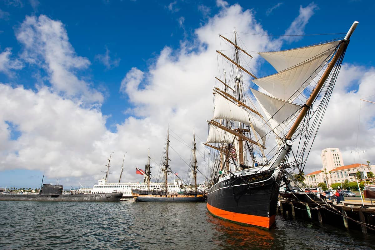 เรือประวัติศาสตร์รวมถึง Star of India จอดเทียบท่าที่ Maritime Museum of San Diego ใต้ท้องฟ้าสีฟ้าสดใสและมีเมฆกระจายอยู่บ้าง