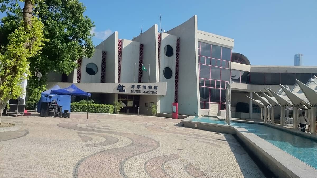 Weitwinkelansicht des Eingangs und der Hauptfassade des Maritimen Museums Macau mit markanter moderner Architektur, runden Fenstern und einem Außenplatz an einem sonnigen Tag.