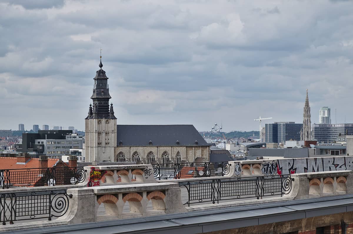 Vista do bairro de Marolles em Bruxelas mostrando a Igreja de Nossa Senhora da Chapelle, grafites nos telhados e o skyline de Bruxelas sob um céu nublado.