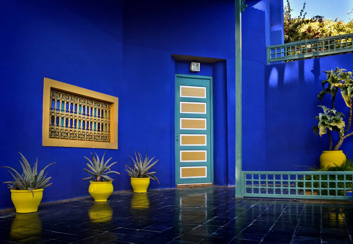 กำแพงสีฟ้าสดใสและสีเหลือง ต้นไม้อวบน้ำในกระถาง และรายละเอียดสไตล์ Art Deco ที่ Jardin Majorelle ในเมือง Marrakech