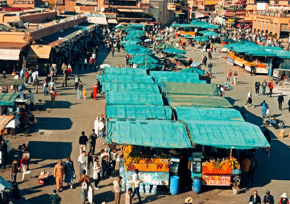 มุมมองทางอากาศของจัตุรัส Jemaa el-Fnaa ในเมือง Marrakech พร้อมแผงตลาดที่มีผ้าใบสีเขียวคลุมและผู้คนเดินอยู่รอบๆ